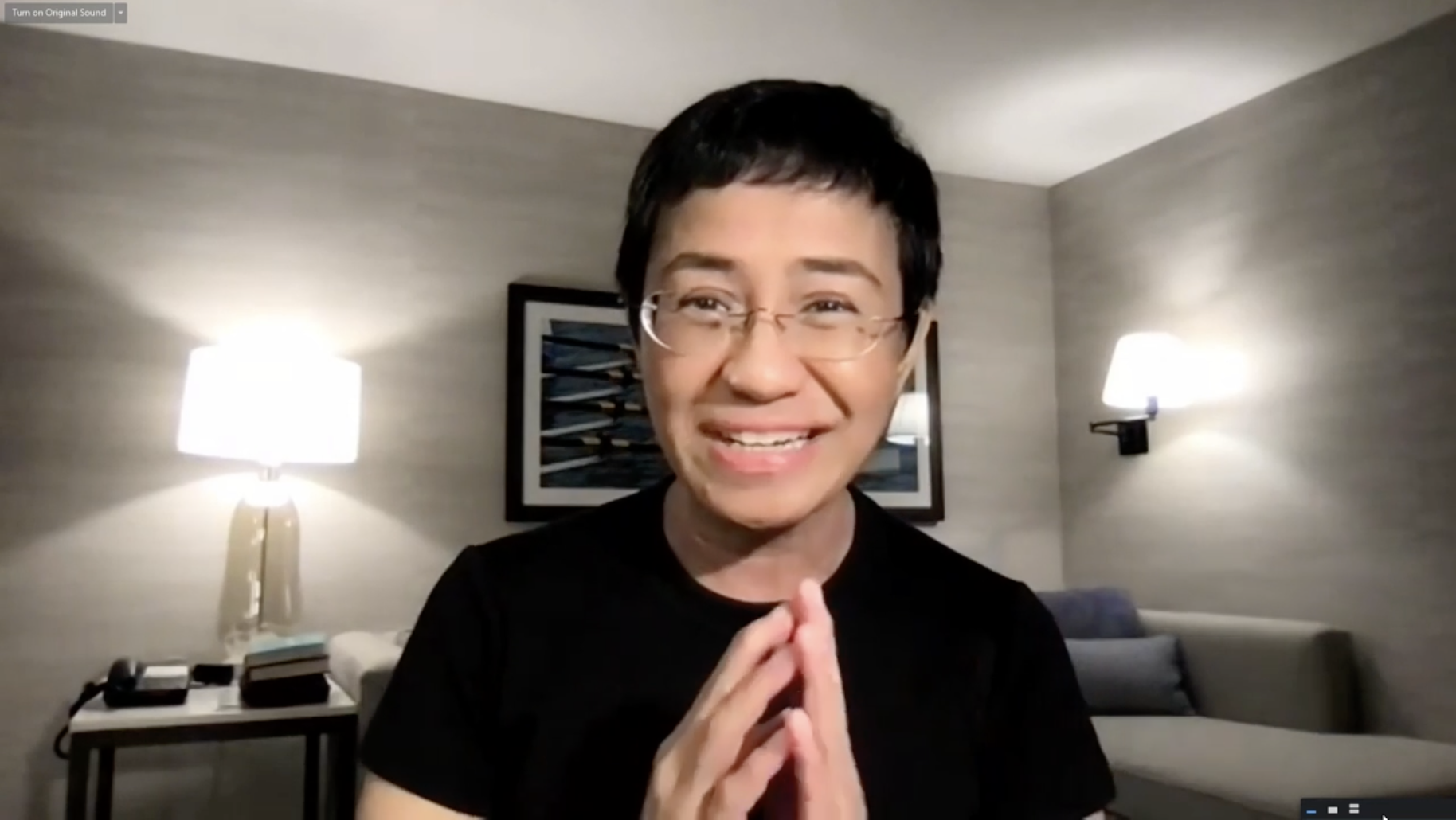 Maria Ressa sitter smilende på sitt hotellrom og holder hendene mot hverandre.