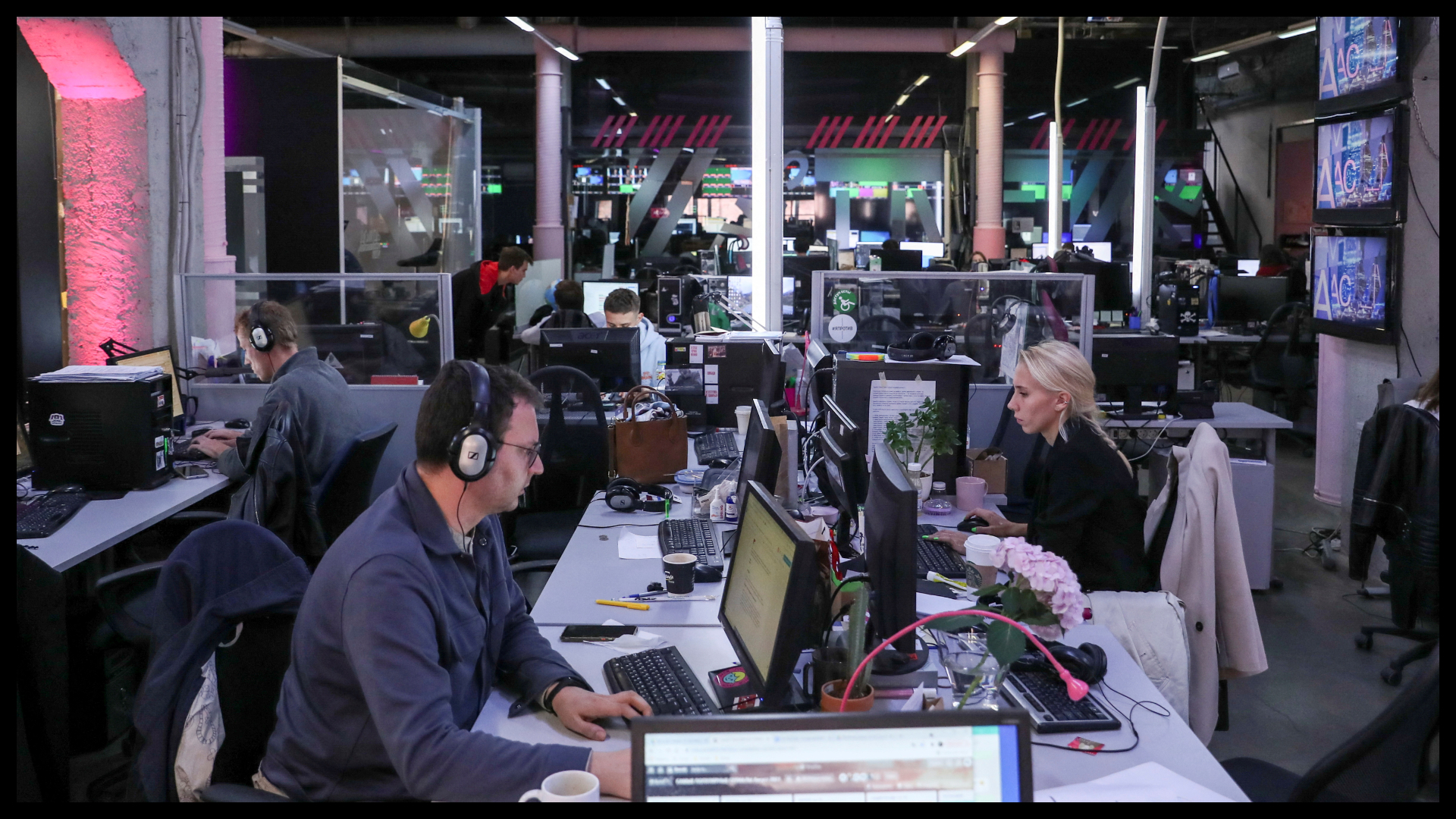 Bilde fra en nyhetsredaksjon i Russland. To journalister sitter på hver sin side av bordet og jobber. I bakgrunnen sees flere journalister i arbeid.