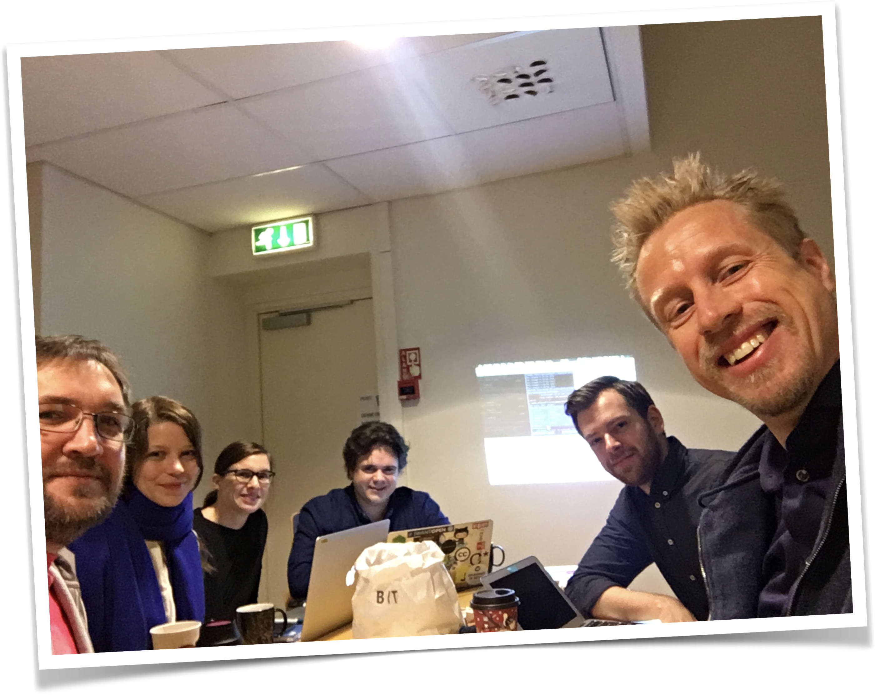 6 smilende kolleger rundt et bord i et møterom.