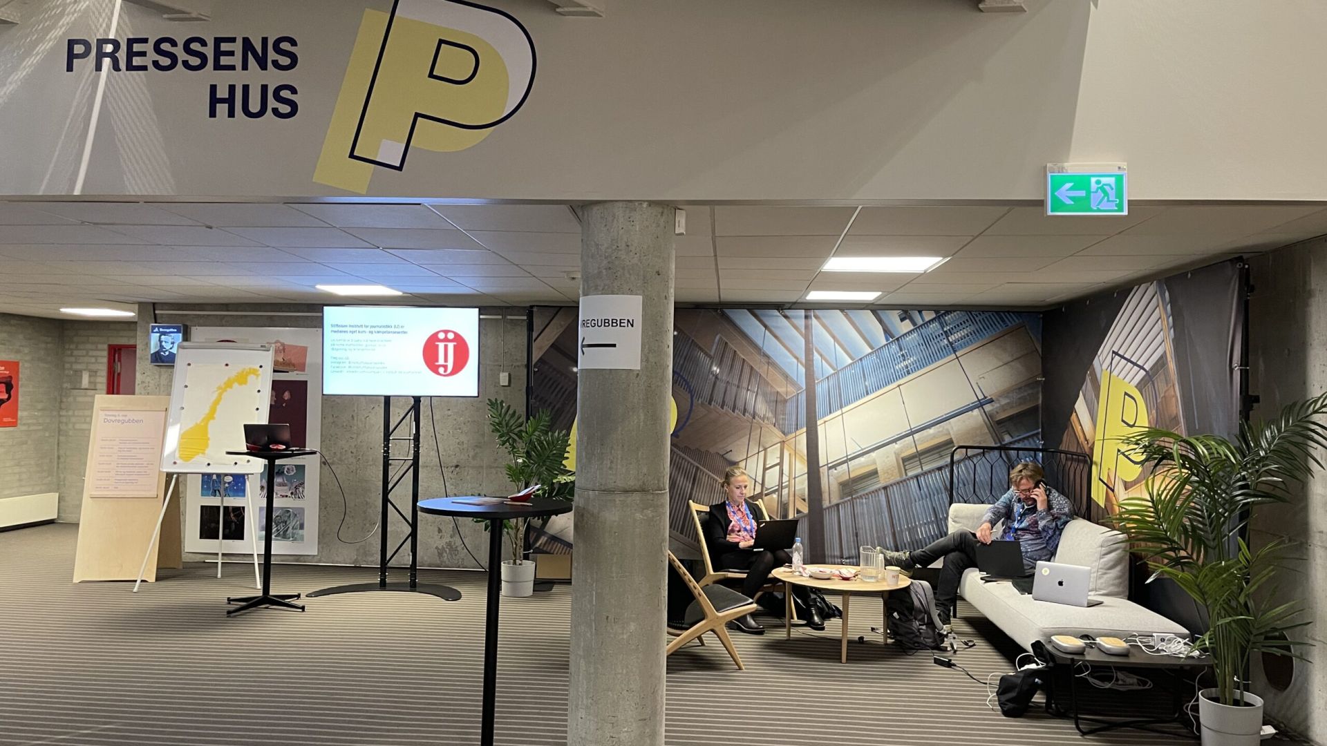 To mennesker sitter og jobber i sofaen i Pressens hus sin lounge under Nordiske mediedager.